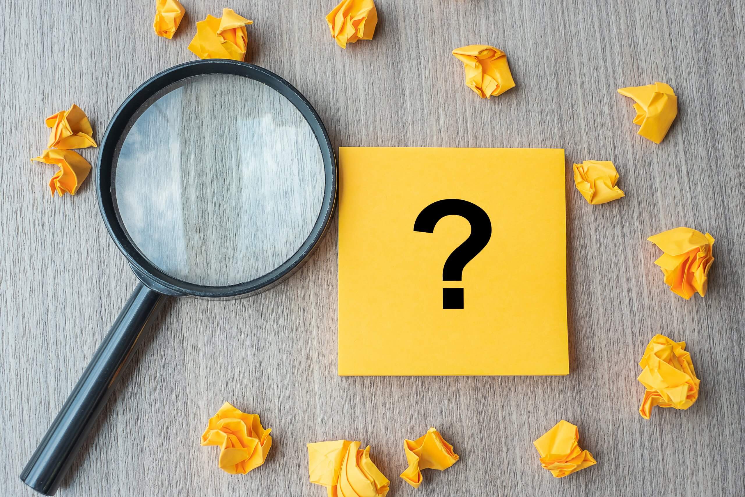 Magnifying glass and sticky note with ? and crumpled sticky notes